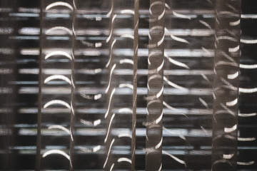 Abstract patterns on a curtain formed by the light entering through narrow holes formed by the exterior wooden shutters.