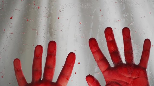 Bloody hands on a white background. Behind a transparent glass covered with red drops. On white background Close up