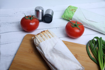 two doner kebabs, onion, salt shaker and tomato on white wooden background