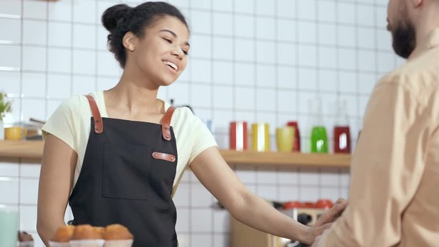 Happy, smiling and friendly afroamerican woman talking with male customer, serving and taking order. Low angle, handheld shot.