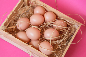 Eggs in the wooden box in the hay on the pink background. Easter concept. Healthy feeding concept. 