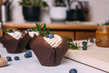 cupcakes with cream and blueberries on kitchen table
