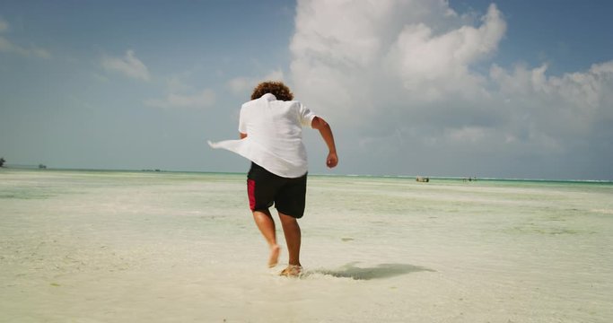 Aerial shot of happy young overweight man is having fun to dancing on a desert beach with clear transparent sea water of a tropical island. Concept of lifestyle, happiness, youth, vacation, holidays 