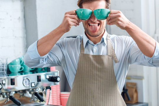 Young adult barista working in coffeeshop, holding cups with beverage in hands
