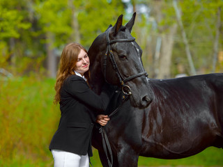 Young girl rider with a black horse in the spring