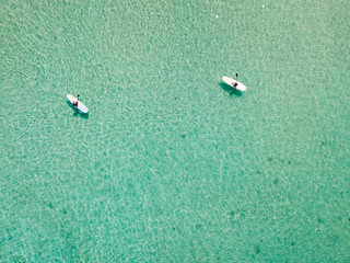 Drone bird eye's view of unidentifiable pair paddle boarding in emerald Caribbean sea