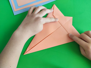 Origami step by step. How to make a paper bunny for Easter greetings and fun. DIY concept. Top view of kids hands making papercraft. Step by step photo instruction 4 out of 11.