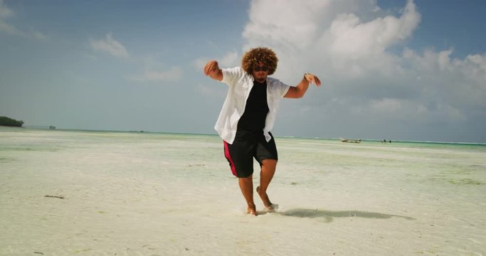 Aerial shot of happy young overweight man is having fun to dancing on a desert beach with clear transparent sea water of a tropical island. Concept of lifestyle, happiness, youth, vacation, holidays 