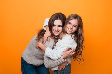 two sisters hugging and having fun in studio on orange background. age difference.