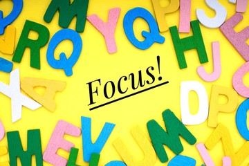 FOCUS text with ABC wooden letters alphabet scattered on a yellow background. Education and copy space