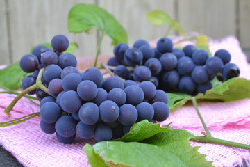 Grapes on a old wooden table. Blue grape and bright leaves on tender pink napkin