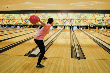 Young woman playing bowling in club. Adult lady spending time enjoying weekend and playing in sport game.