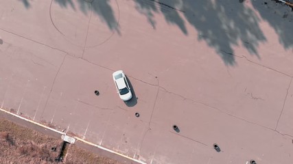 Driver practicing to drive car at abandoned parking lot, aerial drone top view. Car is in abandoned parking lot