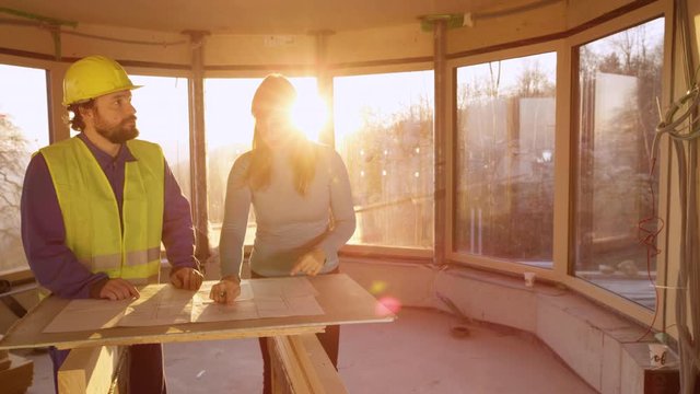 CLOSE UP, LENS FLARE: Angry Caucasian woman reprimands the male static engineer for not working according to the floor plans. Home owner argues with the architect at sunset over the construction plans