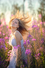 Young beautiful blonde girl gathers pink flowers in the spring blooming field at sunset.