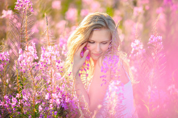 Obraz na płótnie Canvas Young beautiful blonde girl gathers pink flowers in the spring blooming field at sunset.