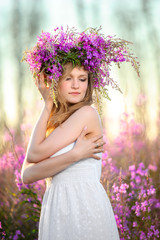 Young beautiful blonde girl gathers pink flowers in the spring blooming field at sunset.