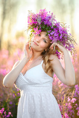 Obraz premium Young beautiful blonde girl gathers pink flowers in the spring blooming field at sunset.
