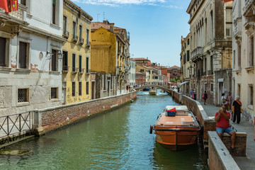 VENICE, ITALY - August 02, 2019: One of the thousands of lovely cozy corners in Venice on a clear sunny day. Locals and tourists strolling along the historical buildings and canals with moored boats