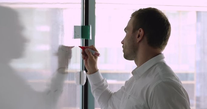 Concentrated young caucasian male manager writing notes on white board.