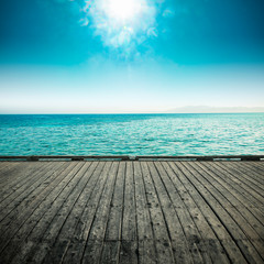 Fototapeta na wymiar gray wooden deck of pier and blue summer sea with sky