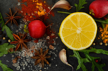 Herbs, spices, lemon, star anise, salton on a black stone background.