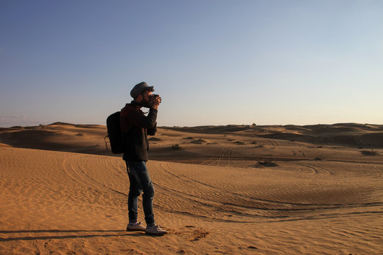 Young man with hat taking photos in the desert