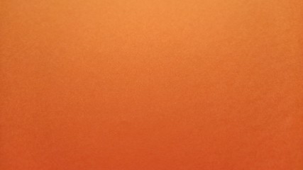 A sheet of thick paper of bright orange color. Close-up. Background intense shade. Natural lateral...