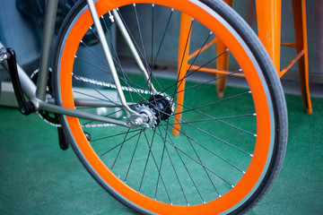 A closeup look at a racing bicycle wheel with an orange frame., in front of an orange metal seat.