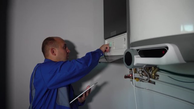 Worker with tablet computer set up central gas heating boiler at home