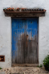 entrance to white house with old wooden door blue, very old and with discoloration, tile roof, plants and mosaic entrance with stones