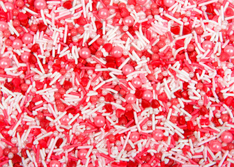 Valentines themed background with red and white candy sprinkles and red heart candies. Flat lay top view from above.