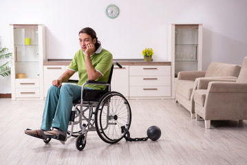 Young male invalid in wheel-chair suffering at home