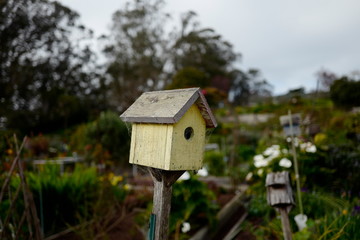 A yellow birdhouse with blurred garden in the background