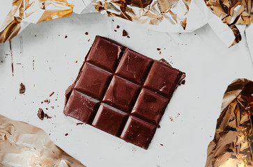 square chocolate bar on dirty white paper with chocolate chips and gold foil around the edges.