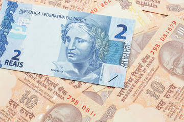 A blue two reais bank note from Brazil close up in macro with a background of United States one dollar bills
