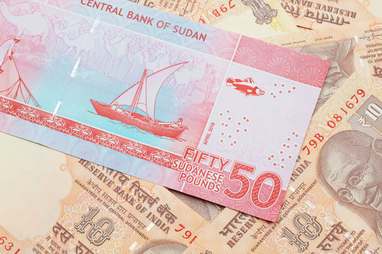 A close up image of a colorful fifty pound bank note from Sudan on a background of Indian ten rupee bank notes