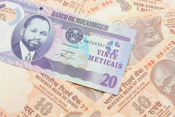 A close up image of a purple, twenty metical bank note from Mozambique on a background of Indian ten rupee bank notes