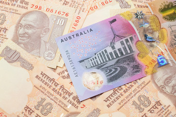 A close up image of an Australian five dollar bill with Indian ten rupee bank notes in macro