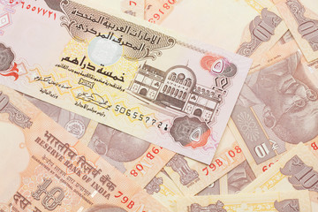 A close up image of a five dirham bank note from the United Arab Emirates on a background of Indian ten rupee bank notes in macro