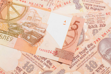 A orange five ruble bank note from Belarus on a bed of Indian ten rupee bank notes close up in macro
