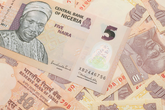 A close up image of a peach colored, five Nigerian naira bank note on a background of Indian ten rupee bank notes