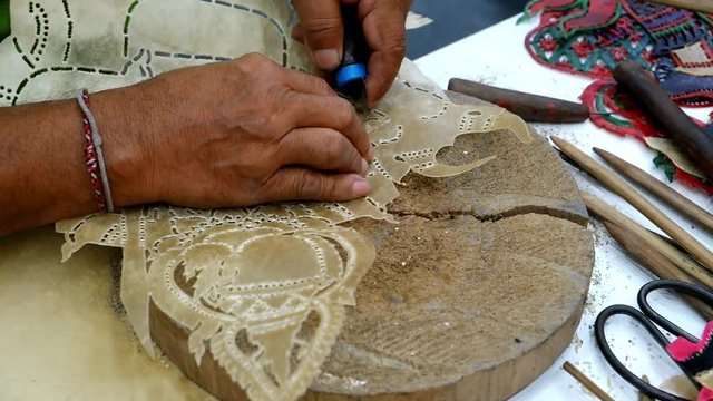 Bangkok,Thailand. Jan 31,2020 : Hands of Thai professional artisan craftsman using tool carving buffalo hide or cowhide leather making traditional handmade handcraft perforated Nang Talung artwork
