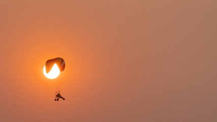 Motor glider with people in the sky along with the sun