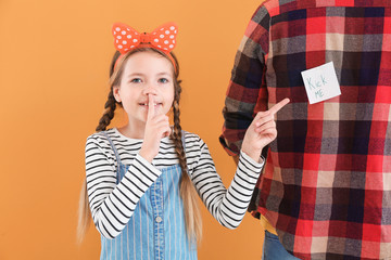 Little girl playing a prank on her father against color background. April Fools' Day celebration