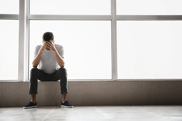 Depressed young man near window