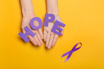 Female hands with word HOPE and violet ribbon on color background. Domestic violence concept