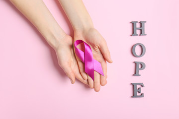 Female hands with violet ribbon and word HOPE on color background. Domestic violence concept