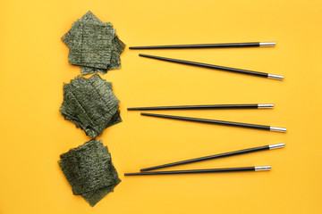 Tasty seaweed sheets and chopsticks on color background