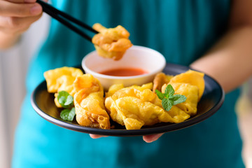 Deep-fried crispy wonton stuffed with minced pork, quail egg and shrimp eating with chili sauce by using chopsticks, Asian food